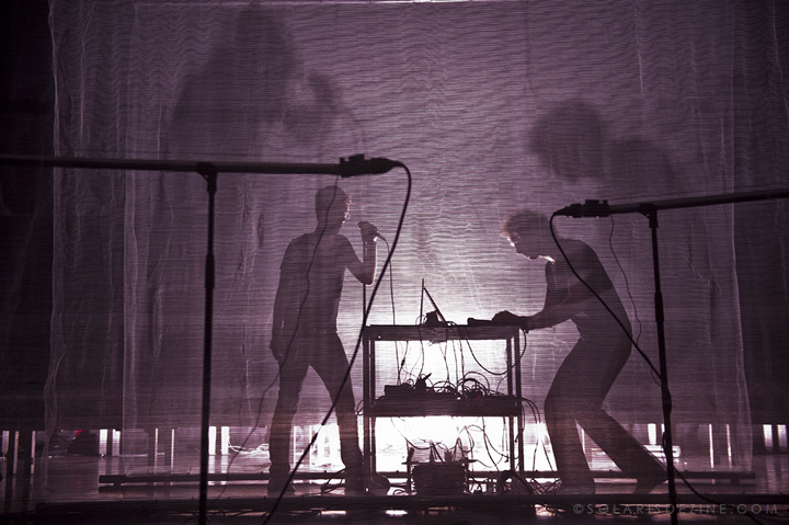 Photo: Marc Solaris. "...interaction between video, sound and movement" Through a stage curtain there is an outline of a person singing into a microphone as an other person controls the mixing console. Article edited by Adriane Kuzminski.