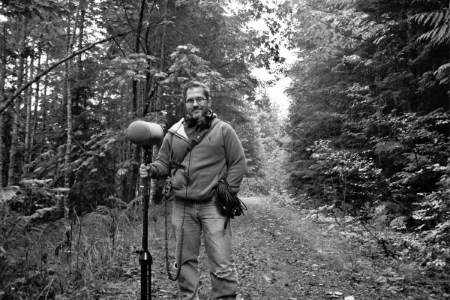 Andy Martin stands with a boom mic and recording gear ready to capture the lush forest surrounding him. Article written by Adriane Kuzminski.