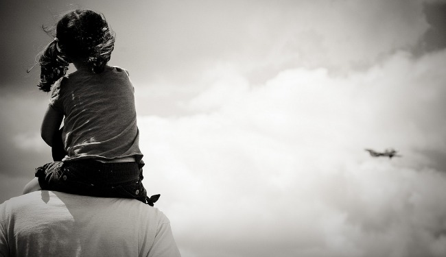 A little girl sits atop her father's shoulders, staring off into the clouds.