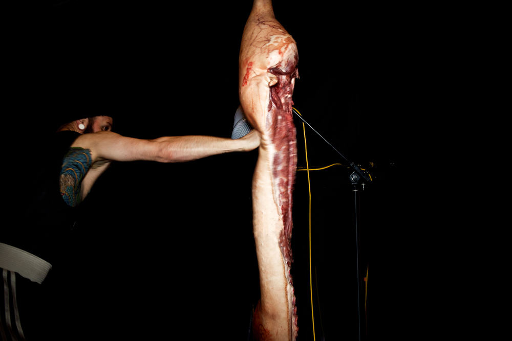 A boxer bare-knuckle punches the meaty spine of pork hanging from the ceiling.