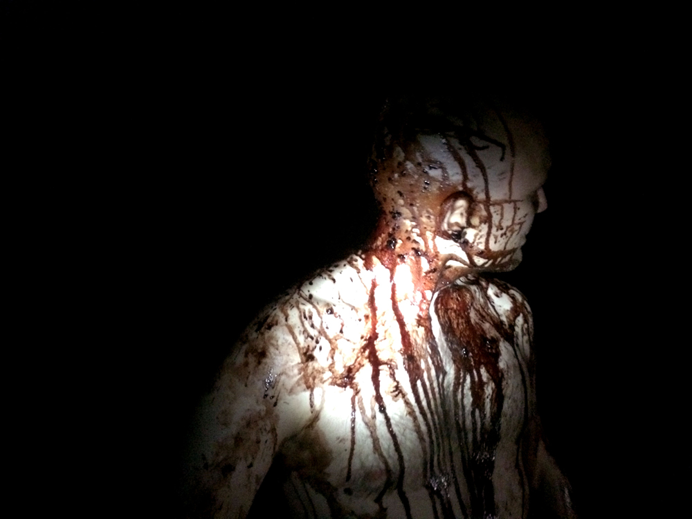 A man stands in the dark covered in pig's blood.