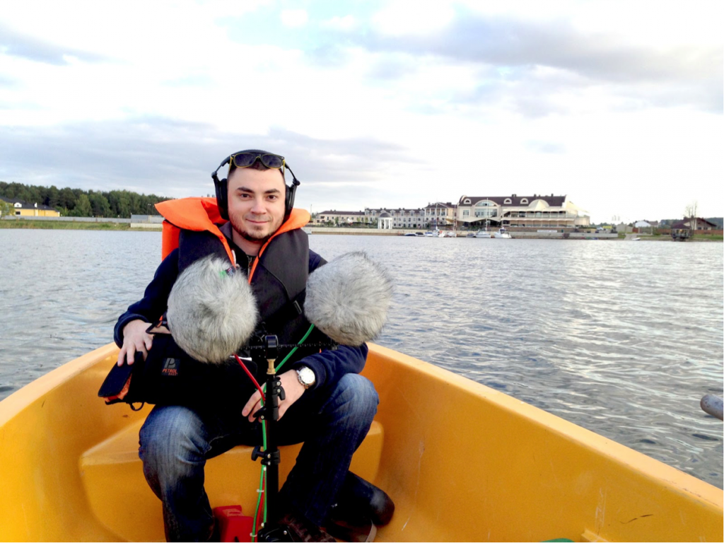 Serj sits in a canoe on a lake with his mic setup.