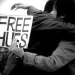 Two people hug with one person holding a free hugs sign.