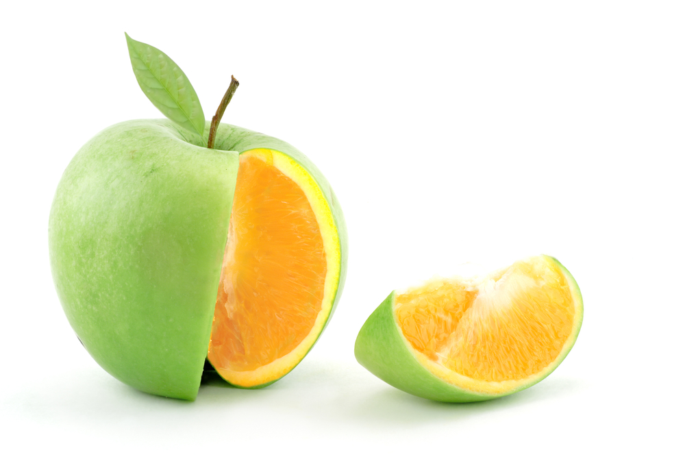 A wedge is cut out of a green apple, revealing the flesh of an orange.