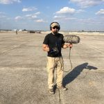 Watson Wu holds a boom mic and gives the thumbs up on the tarmac.